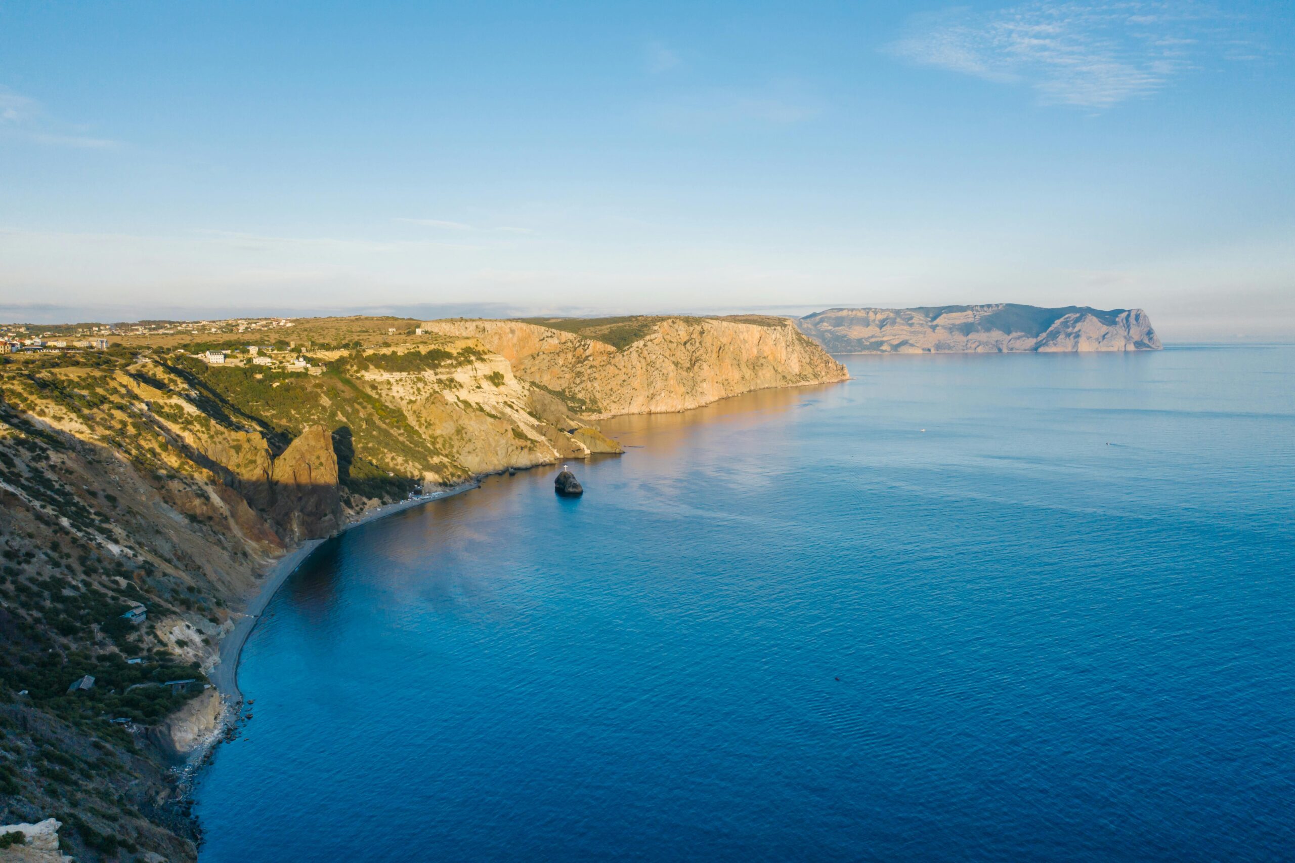 Experience a stunning aerial view of coastal cliffs and calm blue waters under a clear sky.