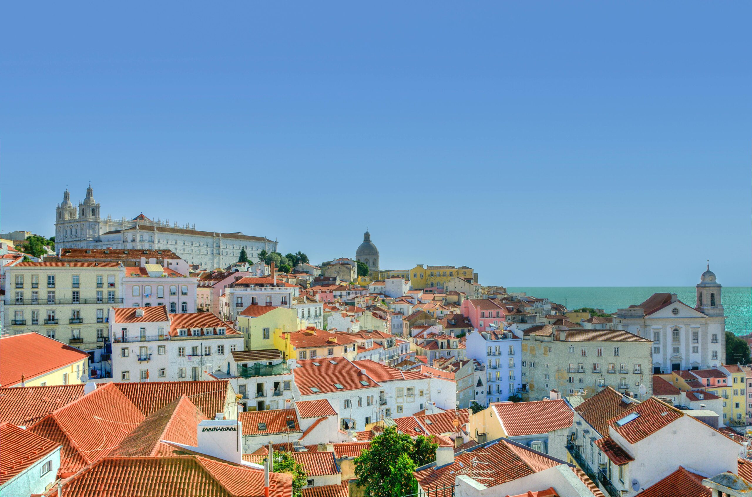 Captivating view of Lisbon's historic architecture with the Atlantic Ocean in the backdrop under a clear blue sky.