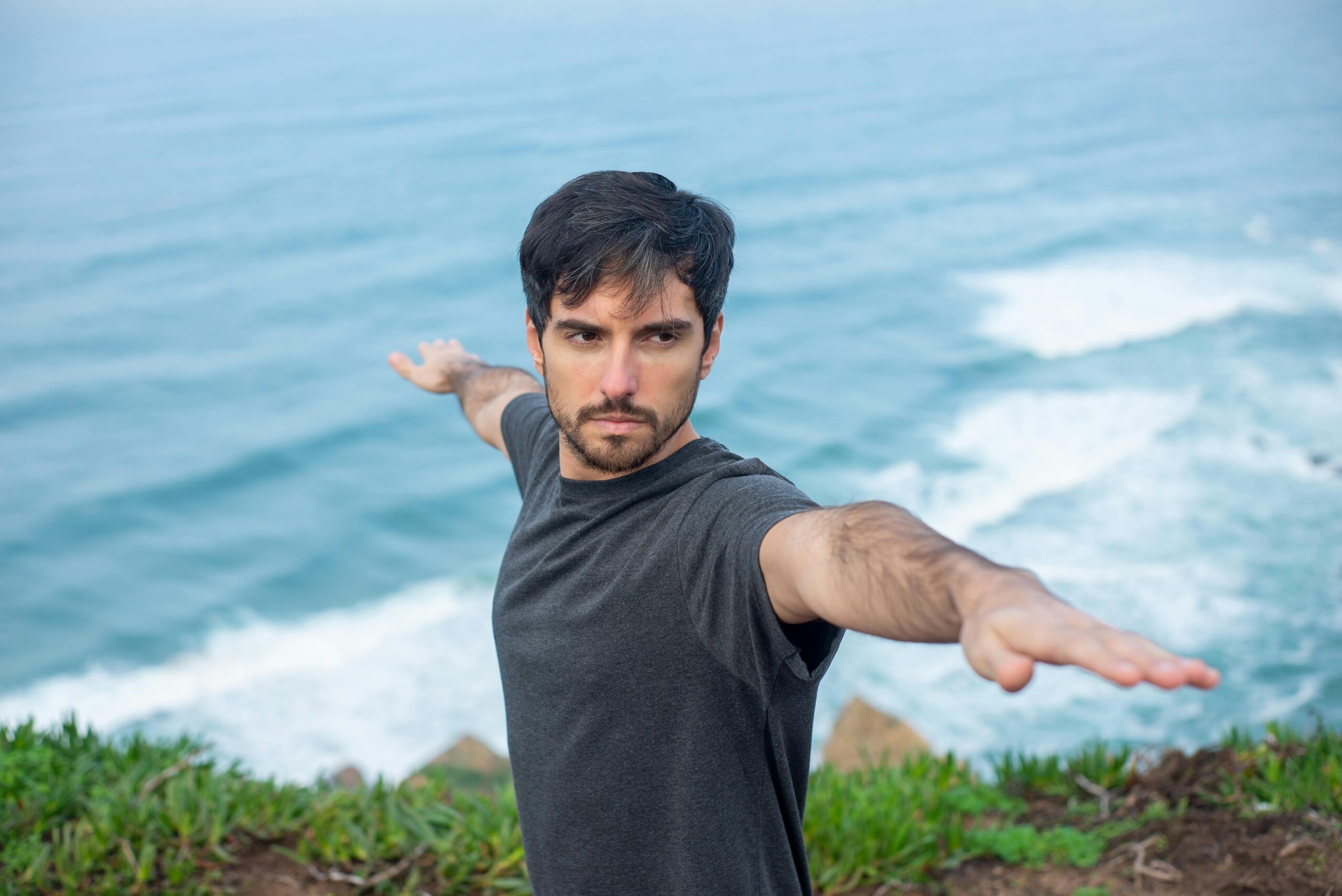 Man performing warrior yoga pose on scenic cliffs by the ocean in Portugal.