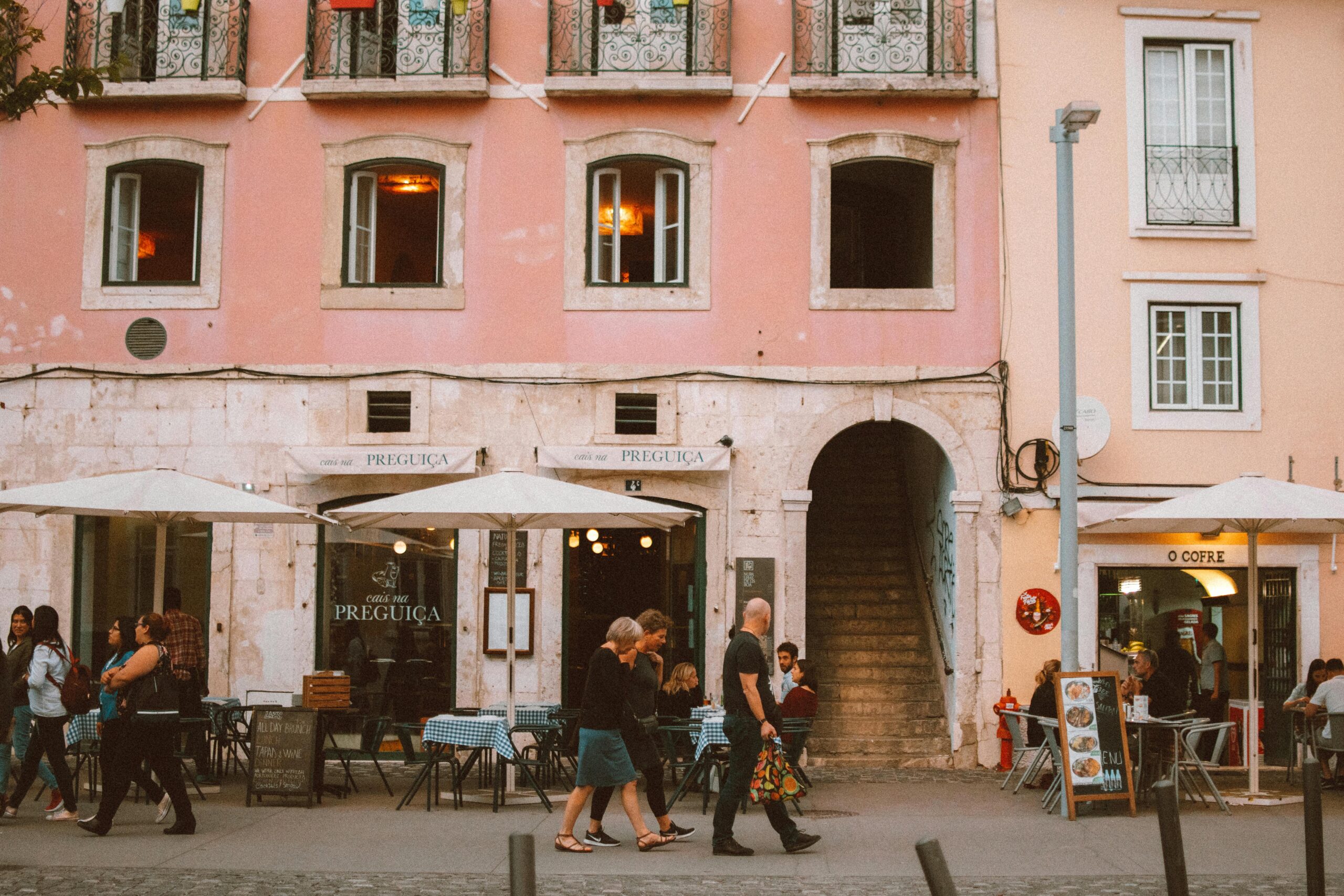 A lively Lisbon street with people passing by cafes and colorful buildings.