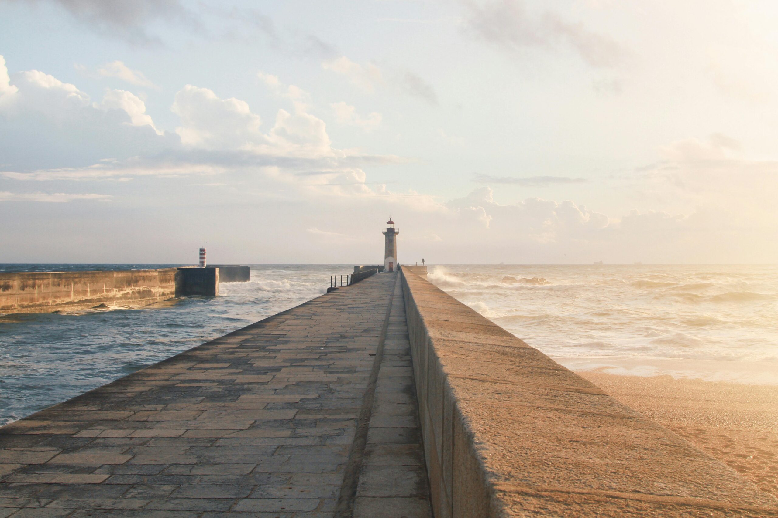 Tranquil view of a lighthouse on a pier by the ocean in Porto during sunset.