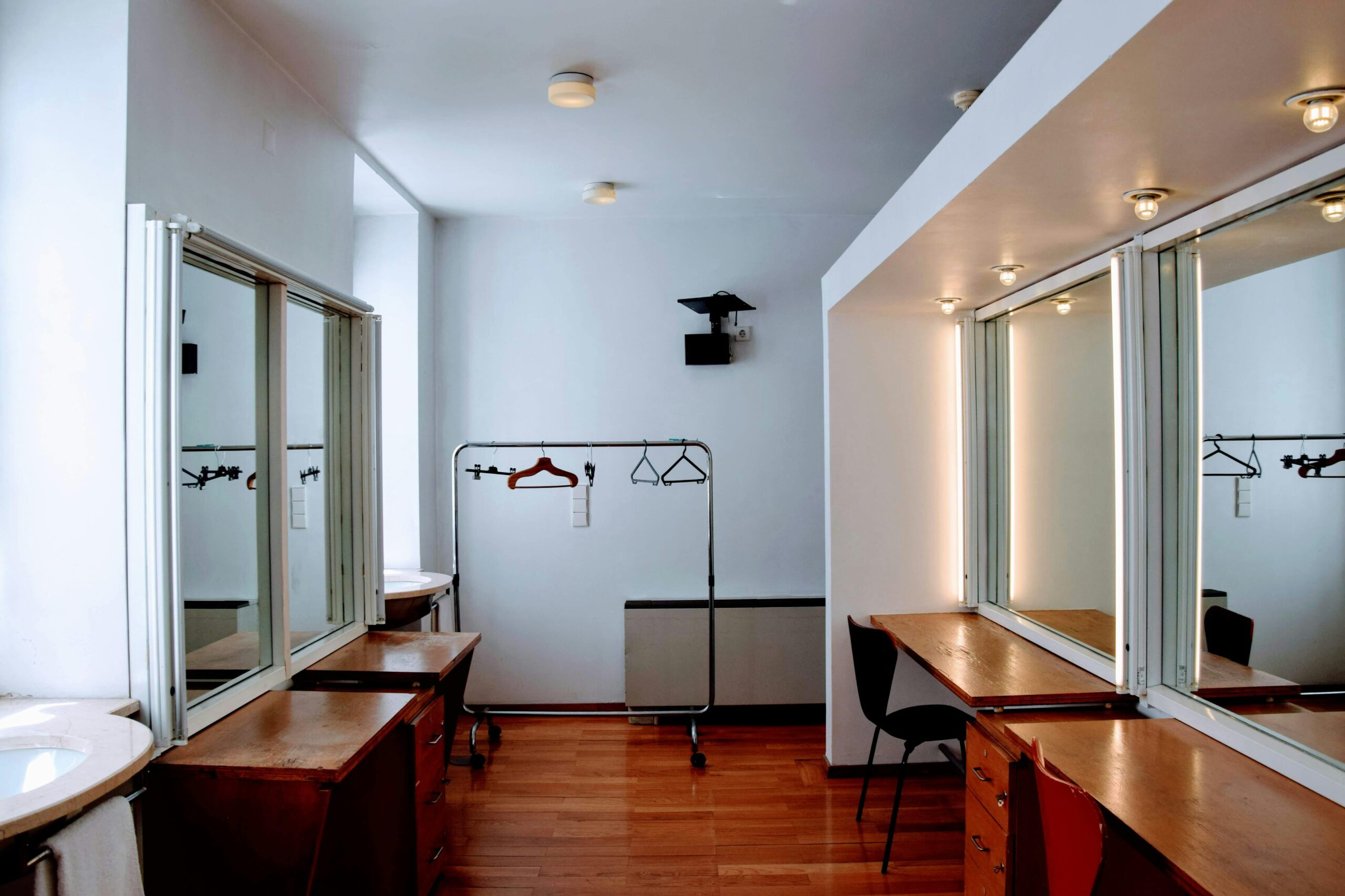 Spacious dressing room with wooden desks, mirrors, and clothing racks.