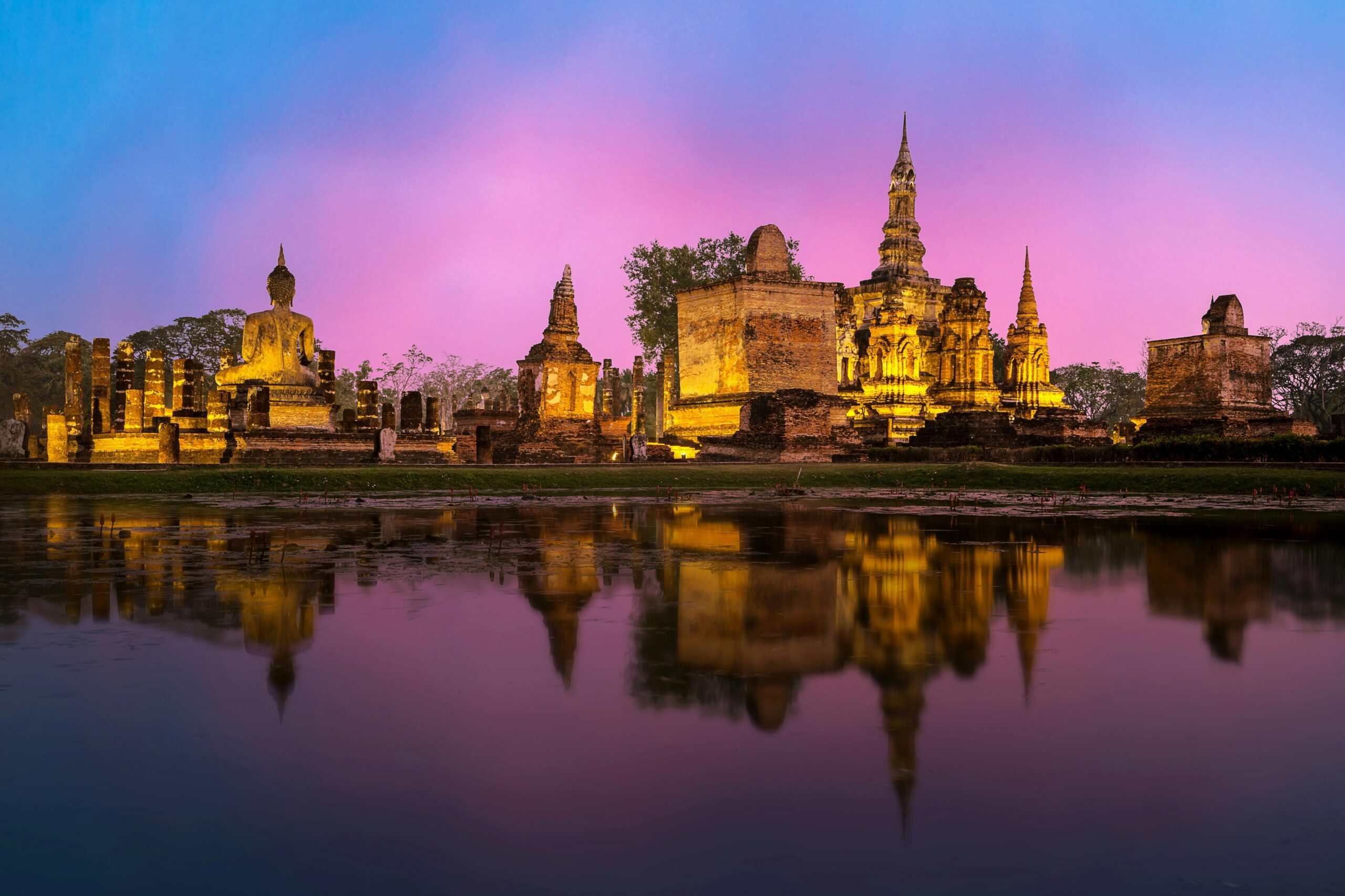 Beautiful sunset view of Wat Mahathat temple in Sukhothai, Thailand, reflecting in the surrounding water.
