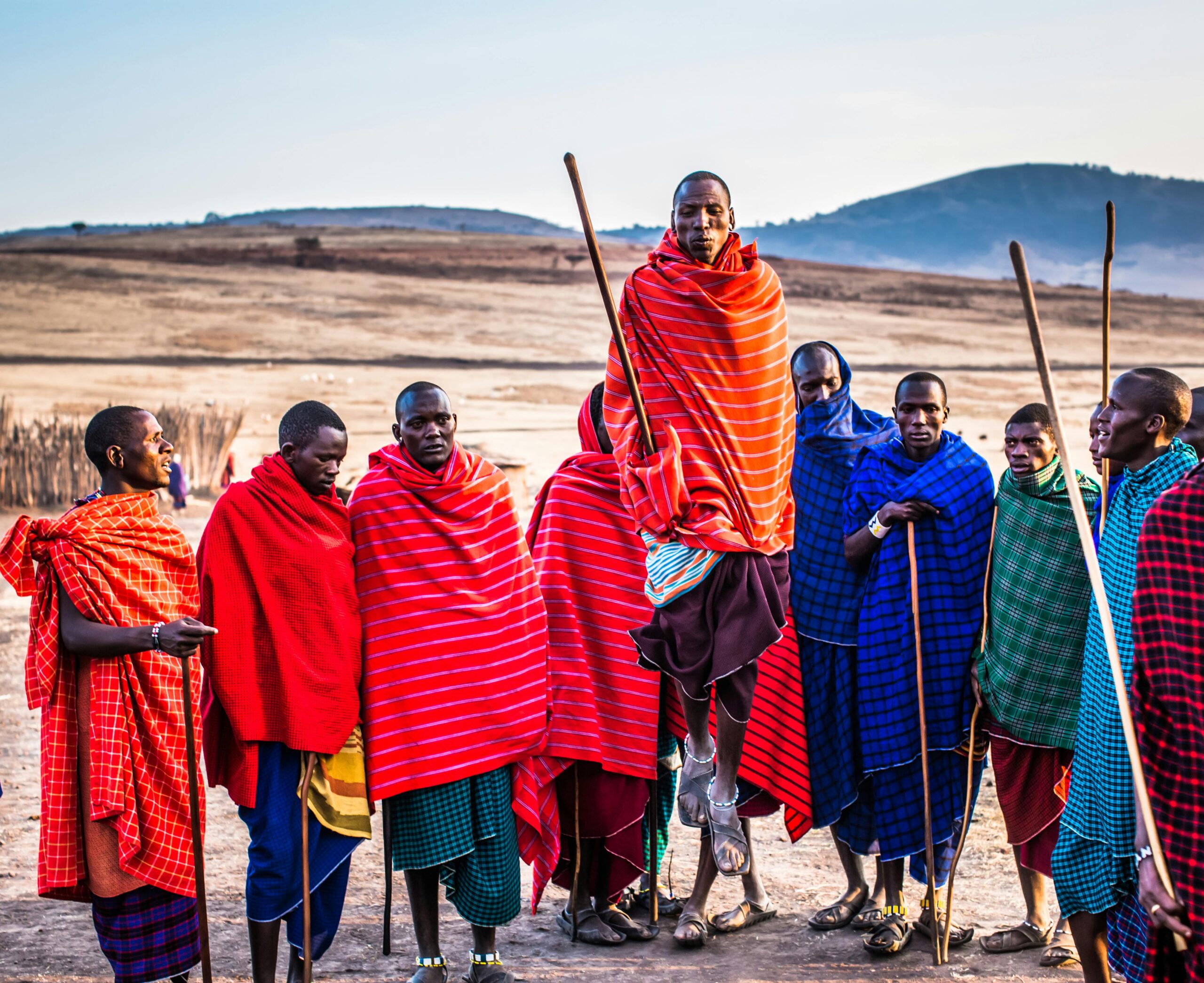 A group of Maasai men in vibrant traditional attire performing a cultural jumping dance outdoors.