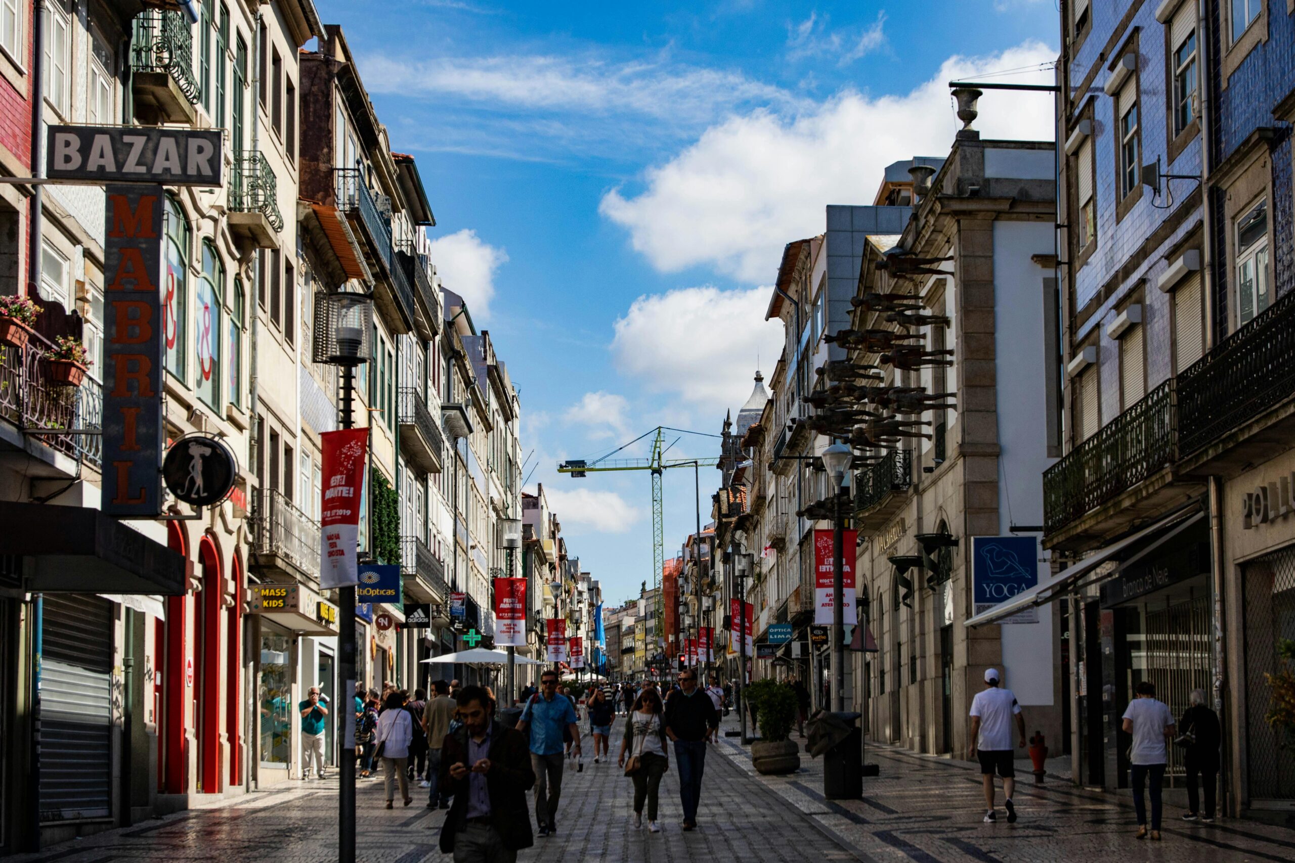 Lively street scene in Porto, Portugal with shops and pedestrians under a bright blue sky.