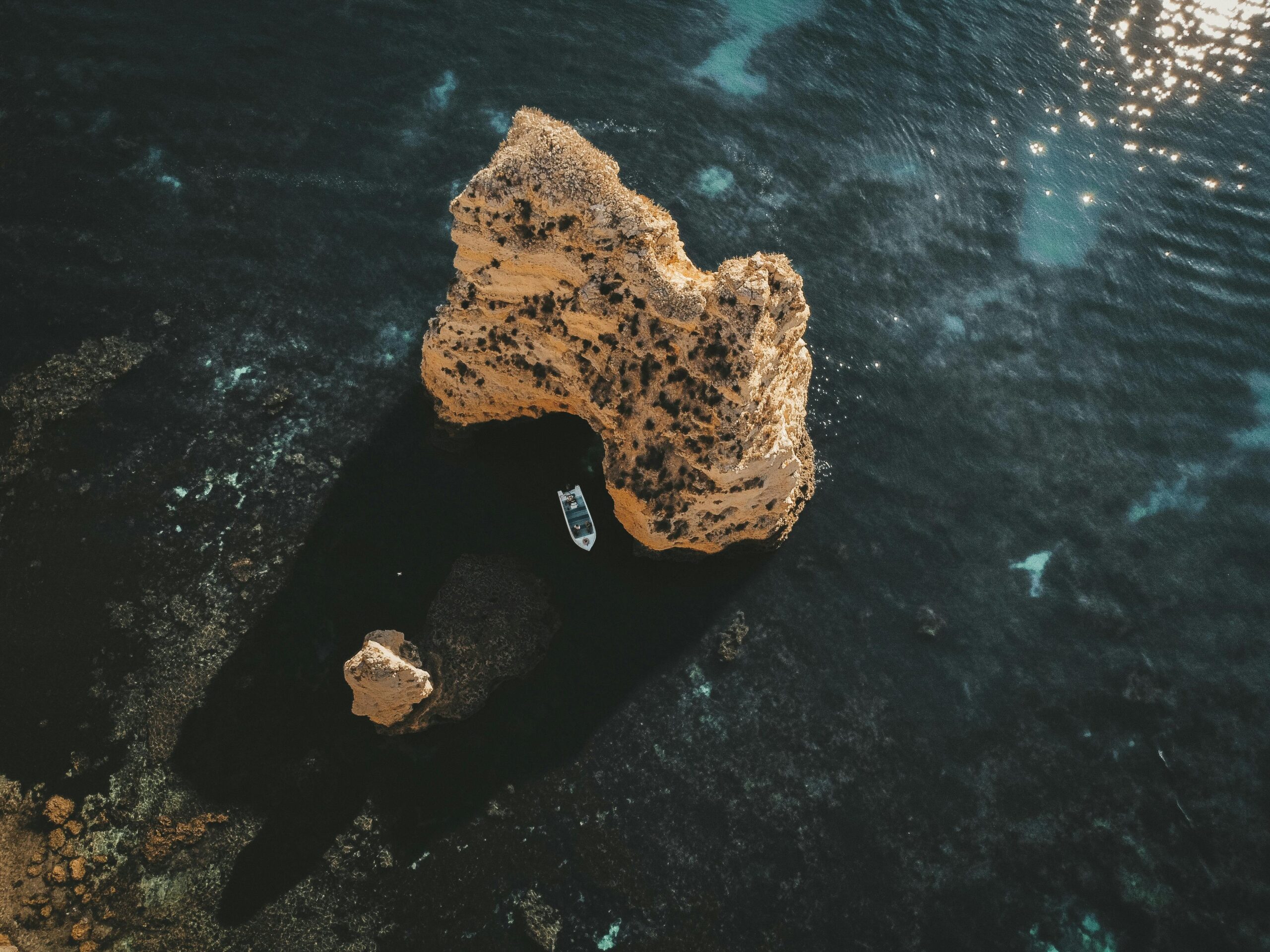 Stunning aerial view of a sea stack and boat in the turquoise waters of Algarve, Portugal.