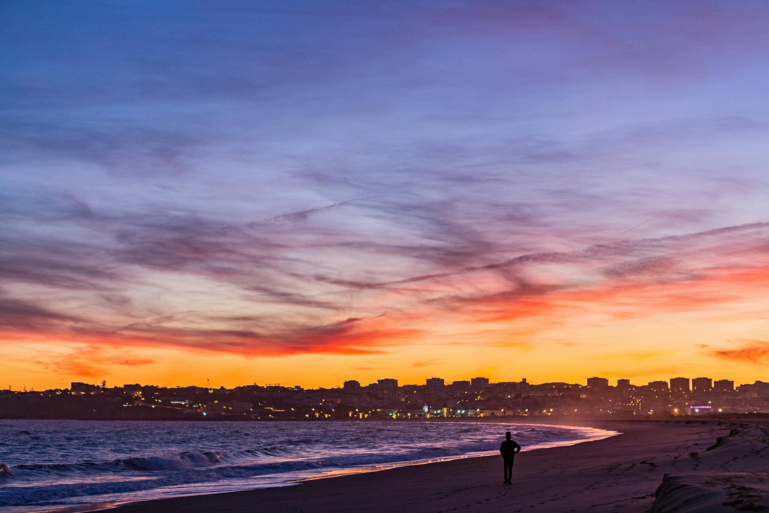 A stunning sunset at Lagos beach, Portugal, with a solitary silhouette and vibrant sky.
