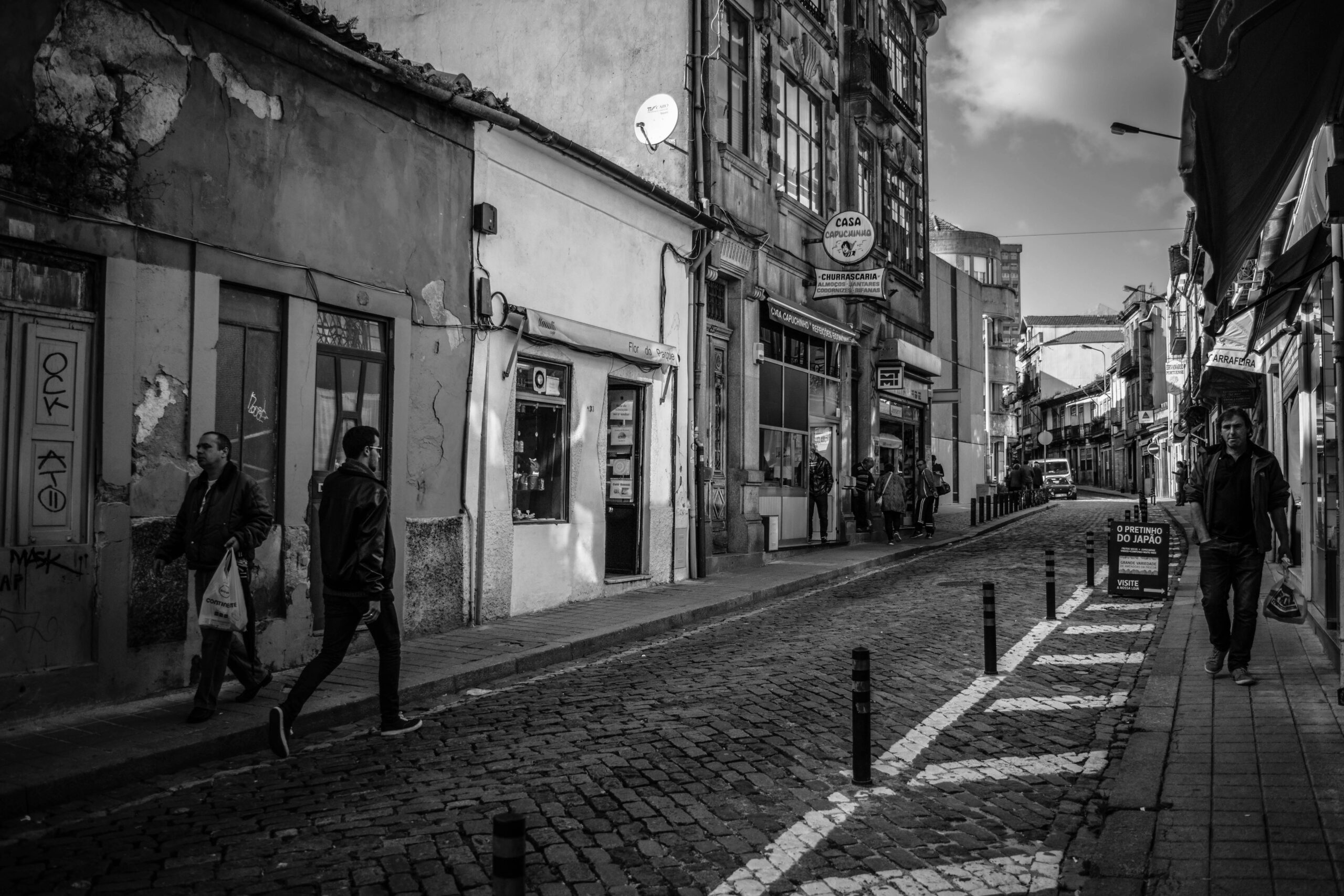 Black and white street scene in Porto, Portugal, showcasing people, shops, and historic buildings.