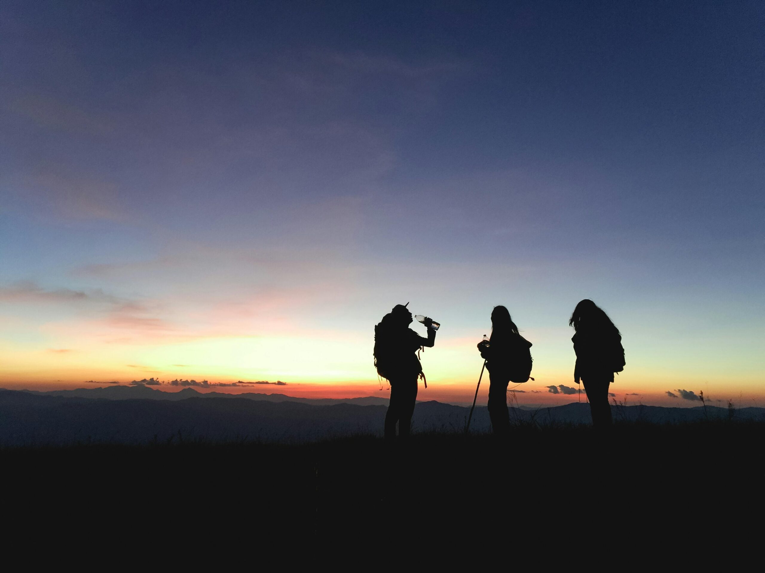Group of hikers silhouetted against a vibrant sunset, enjoying an adventurous outdoor trek.
